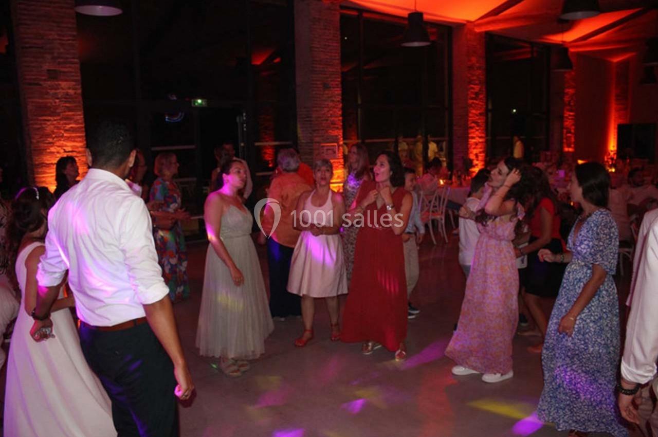 Des personnes dansent et discutent dans une salle éclairée par des lumières colorées lors d'un événement festif.