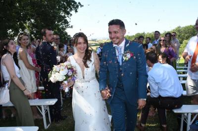 Un couple dans une voiture ancienne quitte un bâtiment entouré de verdure par une journée ensoleillée.