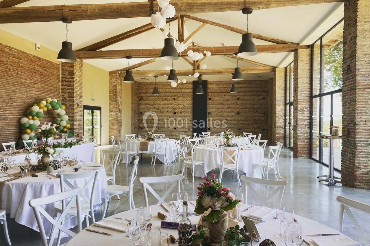 Salle de réception lumineuse avec tables rondes décorées, poutres apparentes et murs en briques.