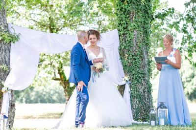 Un couple dans une voiture ancienne quitte un bâtiment entouré de verdure par une journée ensoleillée.