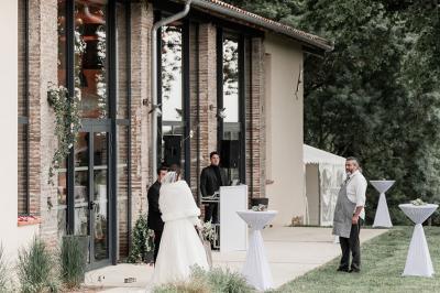 Un couple dans une voiture ancienne quitte un bâtiment entouré de verdure par une journée ensoleillée.