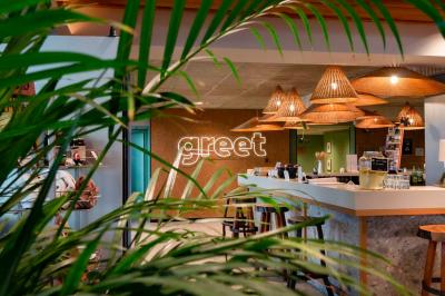 Chambre moderne avec deux lits, mur vert, télévision murale, bouilloire sur étagère et lumière douce.