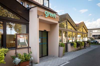 Chambre moderne avec deux lits, mur vert, télévision murale, bouilloire sur étagère et lumière douce.