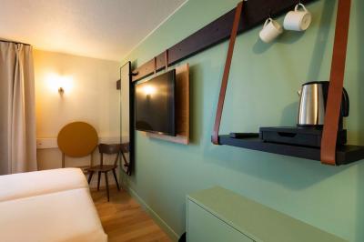 Chambre moderne avec deux lits, mur vert, télévision murale, bouilloire sur étagère et lumière douce.