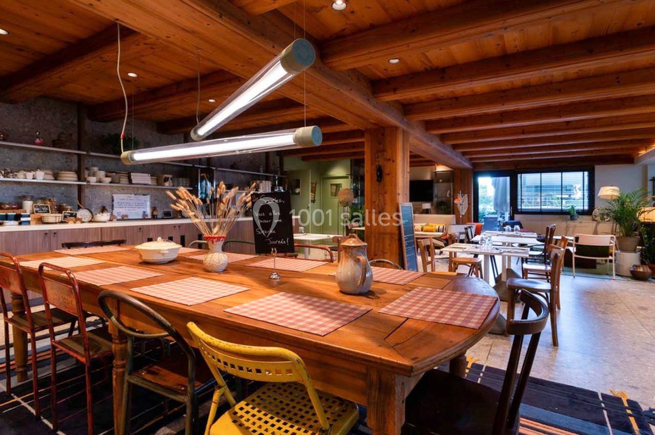 Salle à manger chaleureuse avec grande table en bois, chaises dépareillées, éclairage suspendu et ambiance rustique.