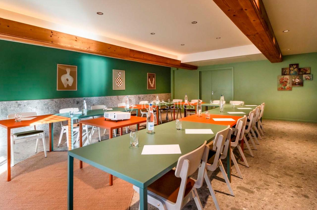 Salle de réunion lumineuse avec tables colorées, chaises en bois, murs verts et décoration murale artistique.