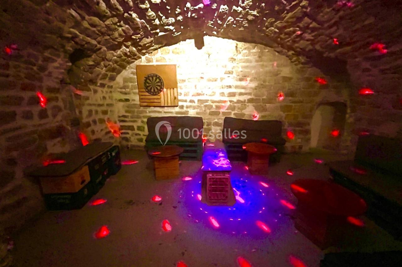 Salle voûtée en pierre avec des canapés, des tables basses et des lumières rouges projetées au plafond et sur les murs.