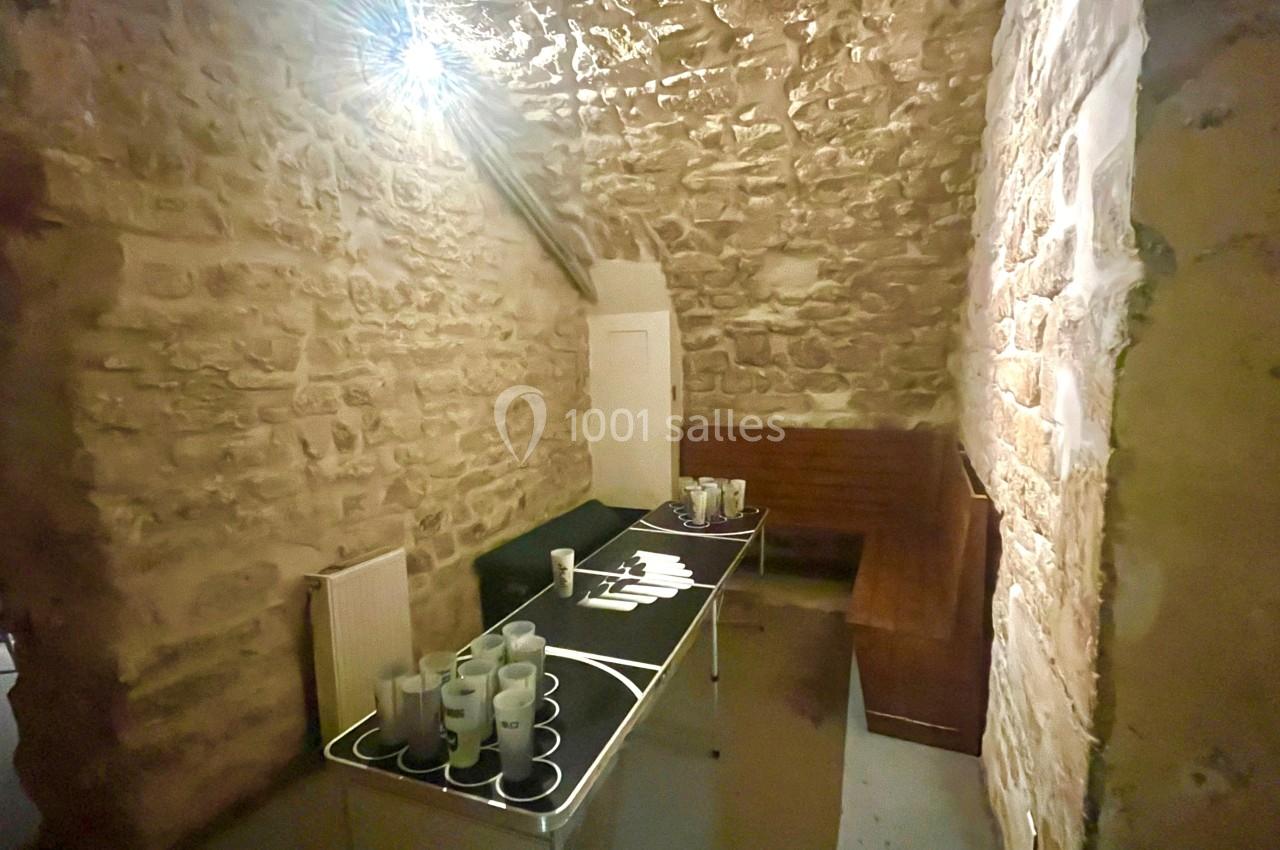 Salle voûtée en pierre avec un comptoir noir, des tasses blanches et un banc en bois contre le mur.