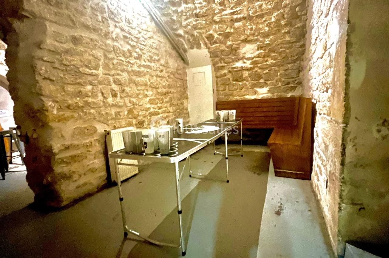 Salle en pierre avec une table pliante équipée de tasses et accessoires, éclairée par une lumière chaude.
