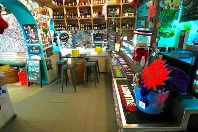 Intérieur d'un bar décoré de fanions, affiches et stickers, avec des tables en bois et des tabourets métalliques.