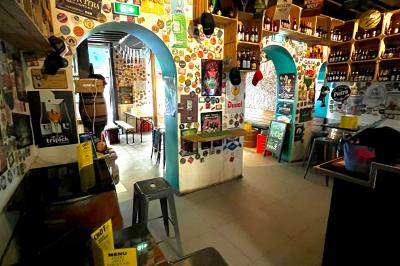 Intérieur d'un bar décoré de fanions, affiches et stickers, avec des tables en bois et des tabourets métalliques.