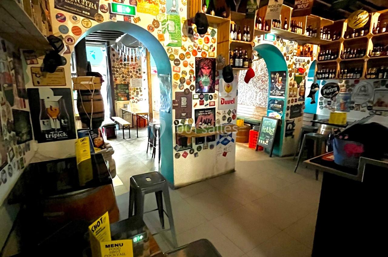 Intérieur d'un bar décoré d'affiches et d'autocollants, avec des étagères remplies de bouteilles et des tabourets…