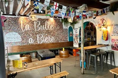Intérieur d'un bar décoré de fanions, affiches et stickers, avec des tables en bois et des tabourets métalliques.