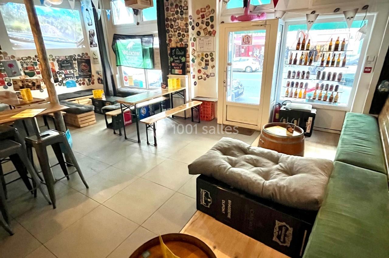 Intérieur d'un bar avec tables en bois, banquettes, décorations murales et étagères remplies de bouteilles.