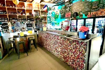 Intérieur d'un bar décoré de fanions, affiches et stickers, avec des tables en bois et des tabourets métalliques.