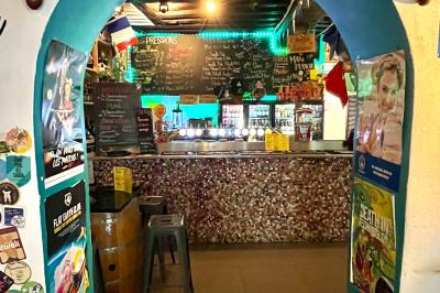 Intérieur d'un bar décoré de fanions, affiches et stickers, avec des tables en bois et des tabourets métalliques.