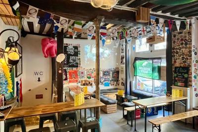 Intérieur d'un bar décoré de fanions, affiches et stickers, avec des tables en bois et des tabourets métalliques.