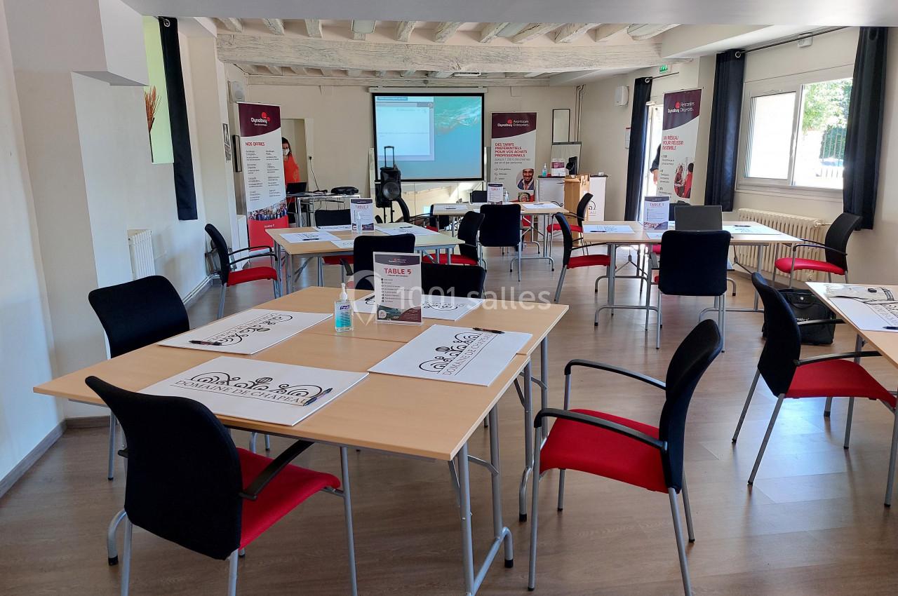 Salle de formation lumineuse avec tables, chaises, documents, écran de projection et affiches promotionnelles.