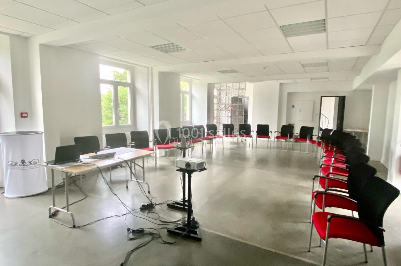 Salle de réunion lumineuse avec des chaises disposées en cercle, un projecteur et une table équipée d'un ordinateur.