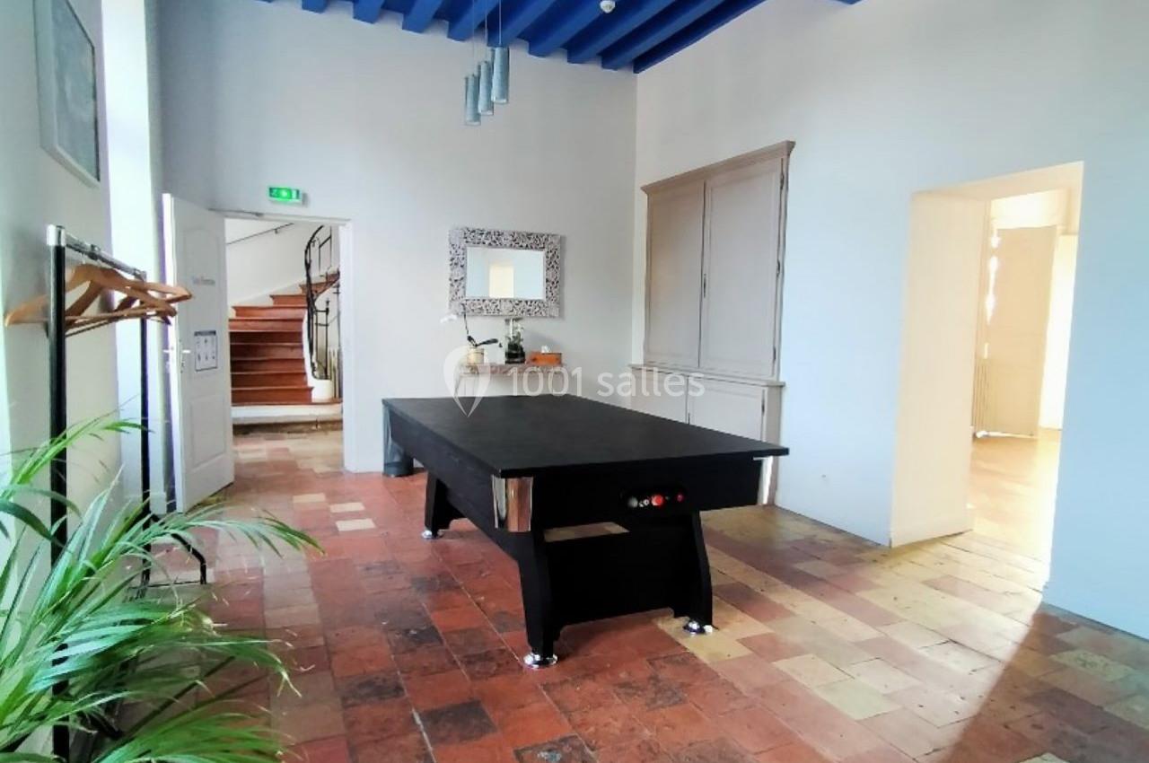 Salle lumineuse avec un billard noir, plafond bleu, sol en carreaux anciens et plantes en décoration.