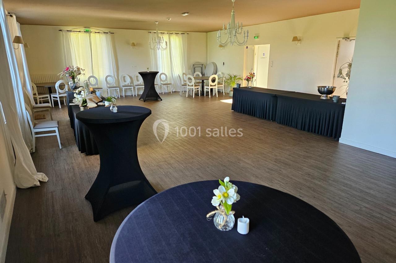 Salle lumineuse avec tables hautes noires, chaises blanches alignées et décoration florale sobre.