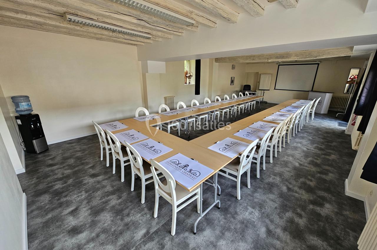 Salle de réunion lumineuse avec tables disposées en U, chaises blanches, projecteur et fontaine à eau.