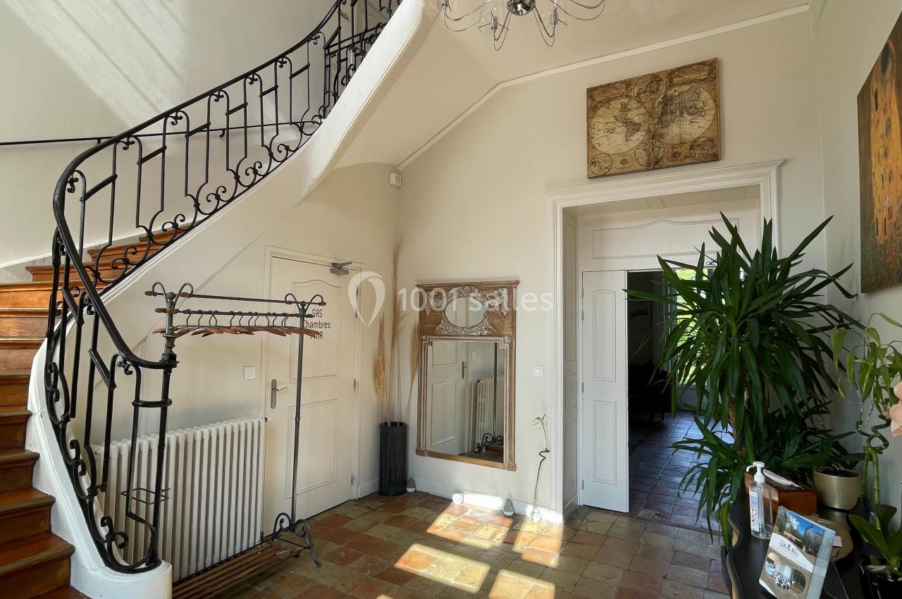 Entrée lumineuse avec escalier en bois, rampe en fer forgé, carrelage ancien et décoration murale.