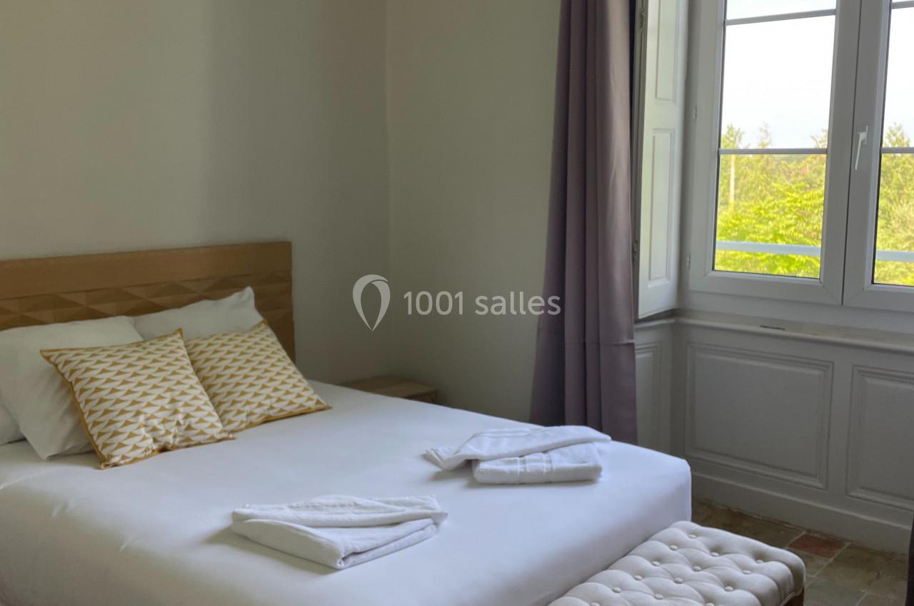 Chambre lumineuse avec un lit double, un banc capitonné, des coussins jaunes et une grande fenêtre donnant sur un paysage…