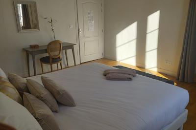 Chambre lumineuse avec un lit double, une grande fenêtre donnant sur un paysage verdoyant, et un fauteuil ancien.