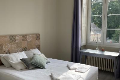 Chambre lumineuse avec un lit double, une grande fenêtre donnant sur un paysage verdoyant, et un fauteuil ancien.