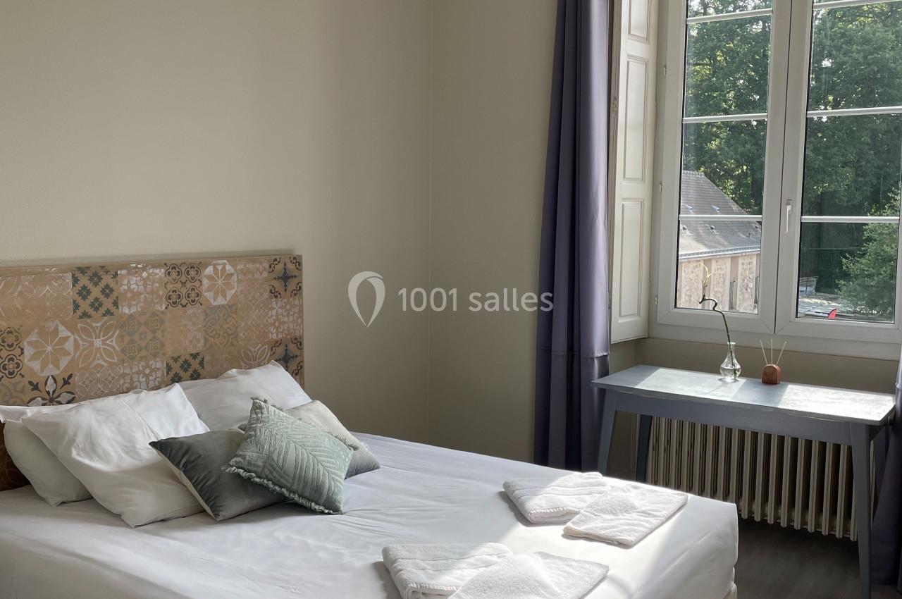 Chambre lumineuse avec lit double, tête de lit décorative, bureau près d'une fenêtre donnant sur un espace vert.