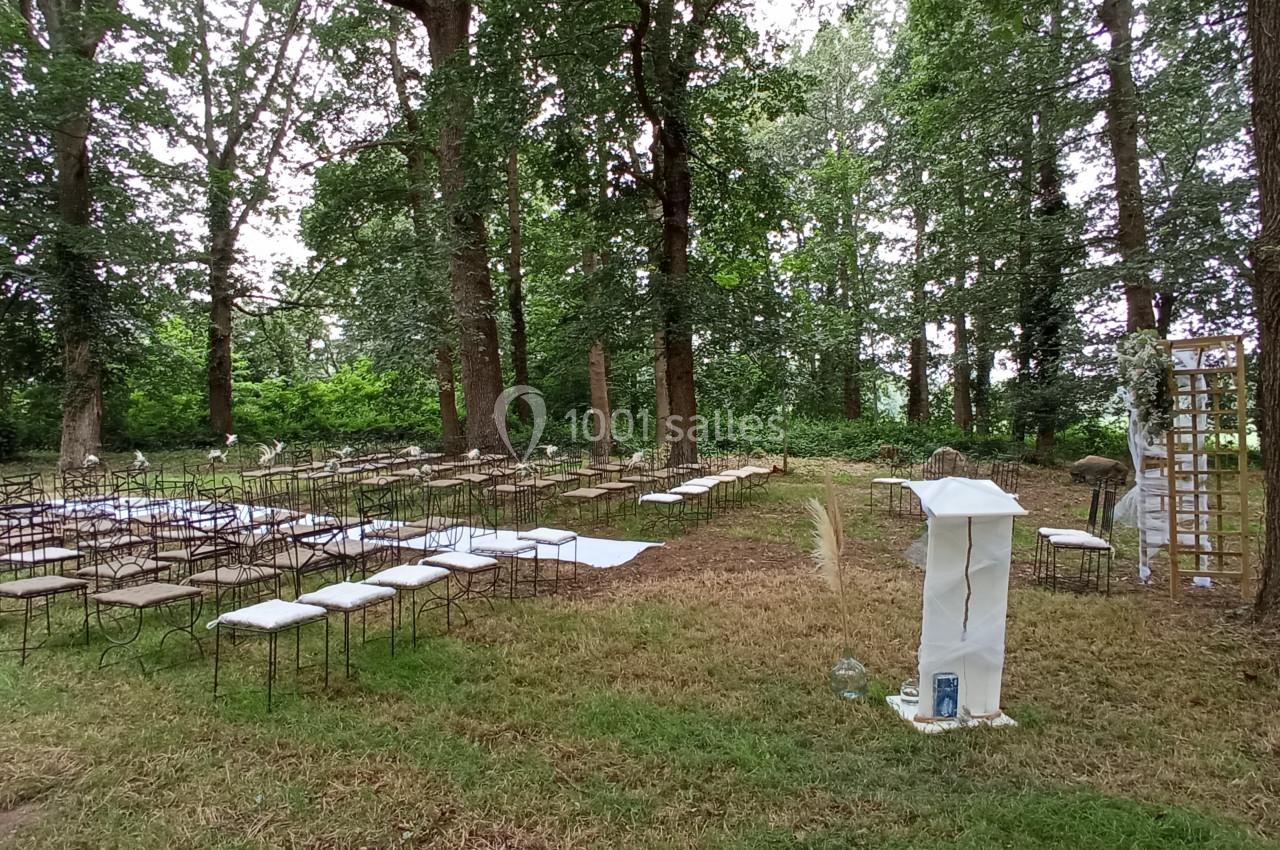 Chaises disposées en rangées et pupitre décoré dans une clairière boisée, préparés pour une cérémonie en plein air.