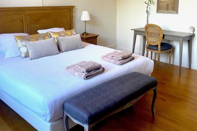 Chambre lumineuse avec lit double, banc capitonné, bureau en bois, lampe et miroir sur un parquet en bois clair.