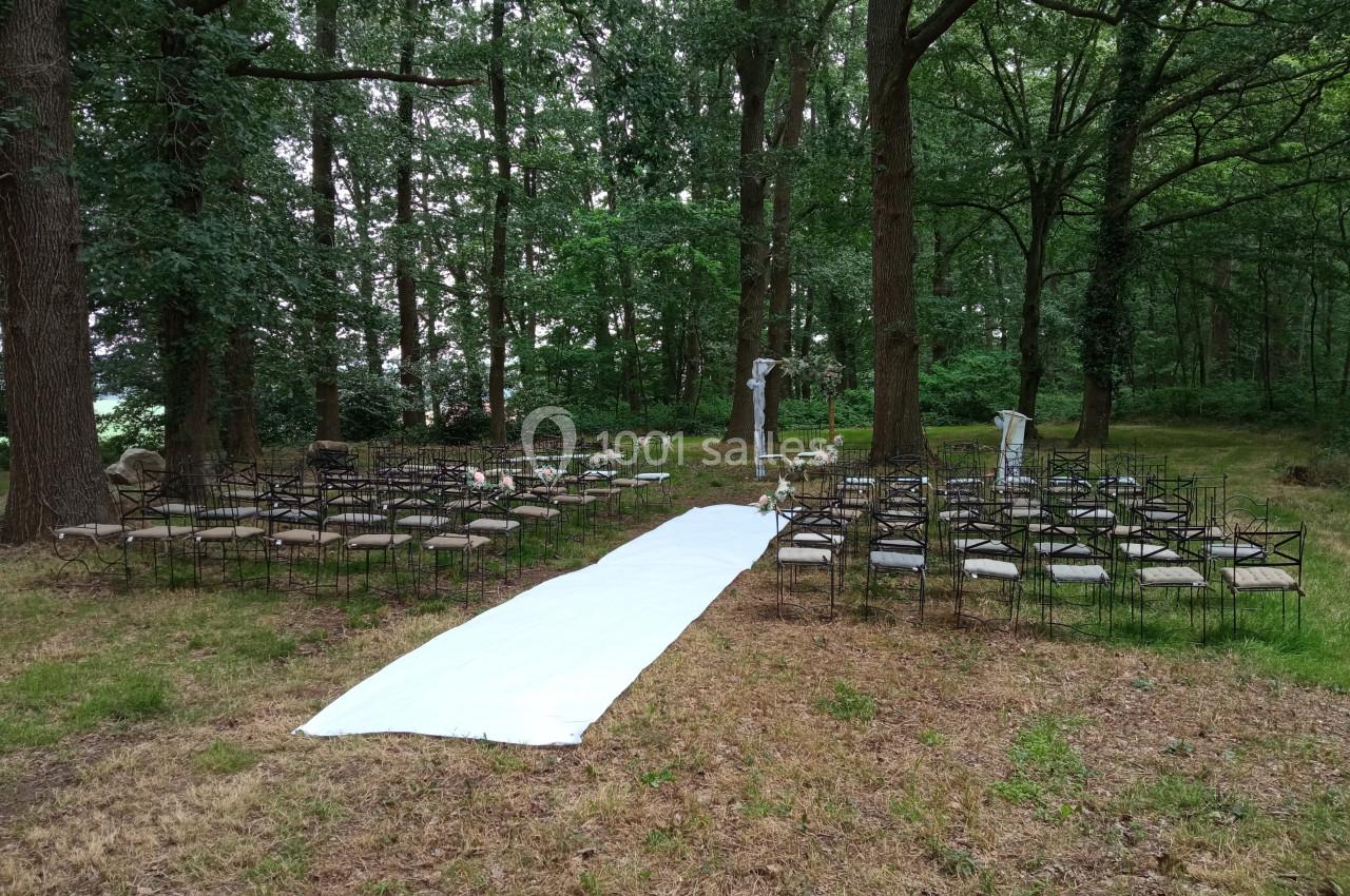 Allée blanche menant à des chaises disposées en extérieur dans une clairière boisée pour une cérémonie.