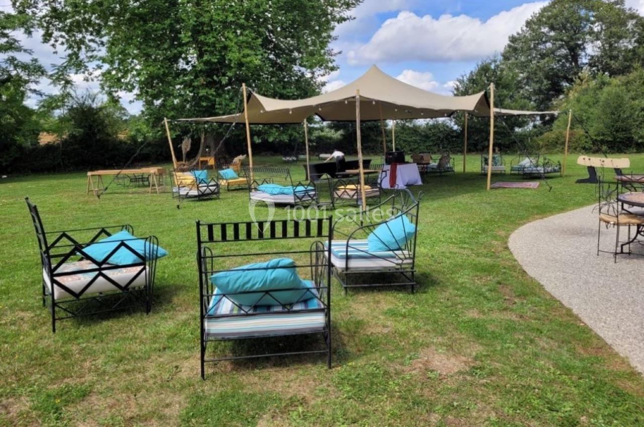 Chaises et tables disposées sur une pelouse avec une tente beige en arrière-plan, dans un cadre extérieur verdoyant.