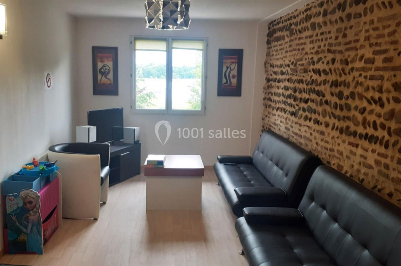 Salle d'attente lumineuse avec canapés noirs, table basse, jouets pour enfants et mur en pierres apparentes.