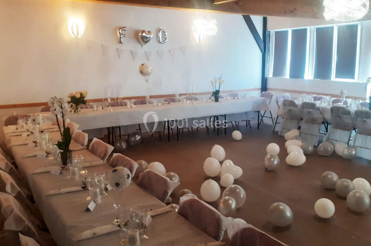 Salle décorée pour un événement avec tables dressées, ballons blancs au sol et guirlande de lettres argentées.