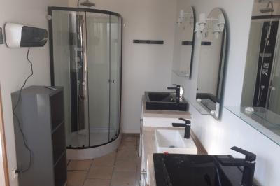 Salle de bain avec douche arrondie, deux lavabos noirs et blancs, miroirs et étagères murales.