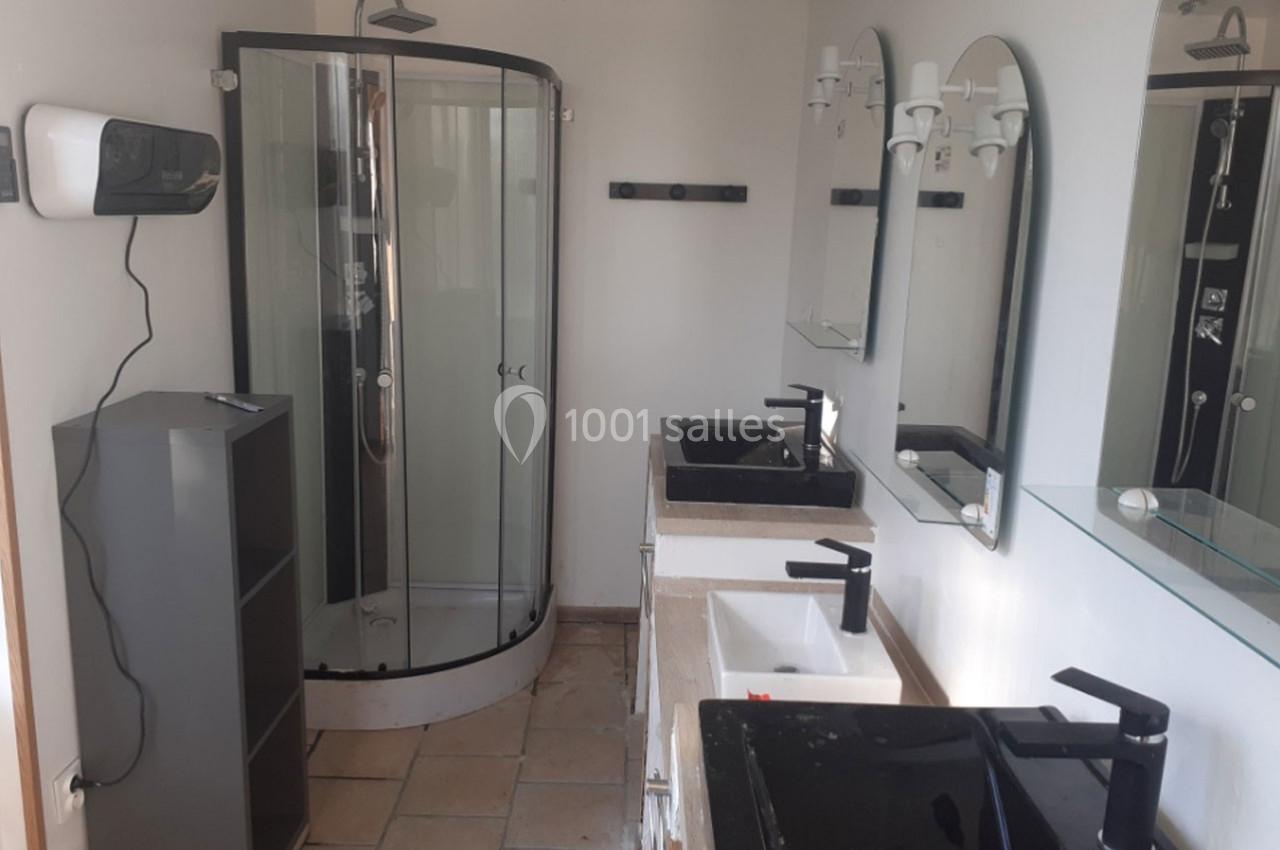 Salle de bain avec douche arrondie, deux lavabos noirs et blancs, miroirs et étagères murales.