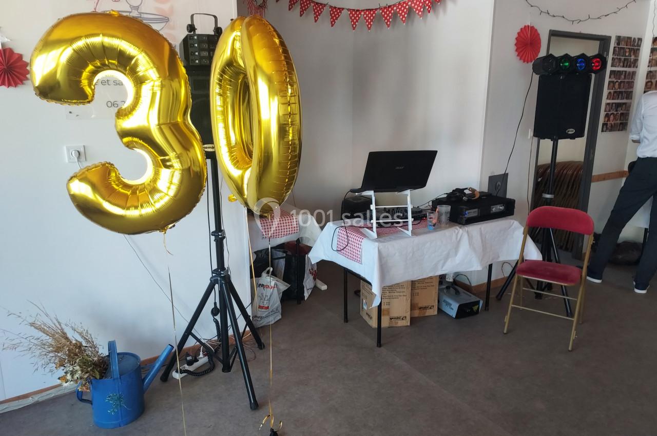 Deux ballons dorés en forme de ’30’ dans une salle décorée pour une fête, avec table de DJ et guirlandes.