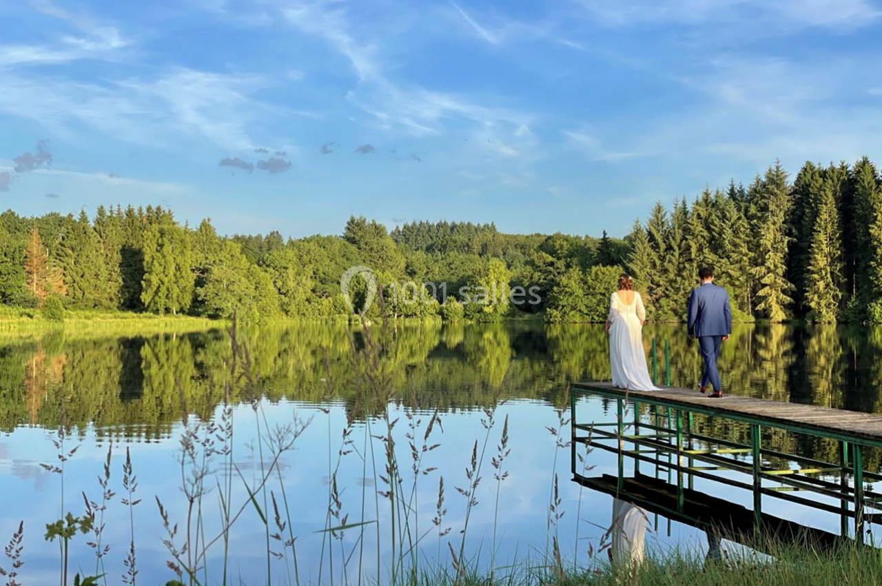 Un couple marche sur un ponton en bois au bord d'un lac entouré de forêt sous un ciel bleu.