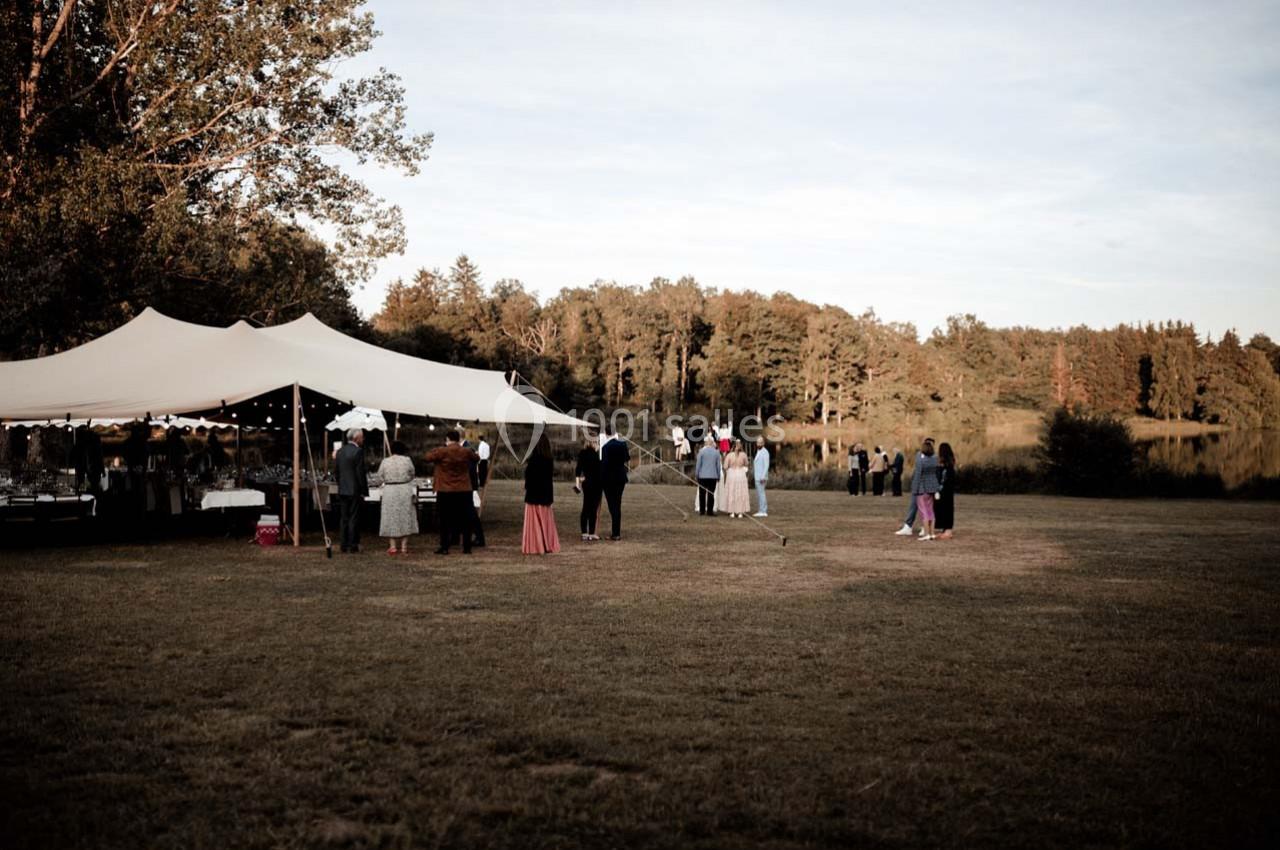 Personnes rassemblées près d'une tente blanche dans un espace extérieur verdoyant, entouré d'arbres au coucher du soleil.