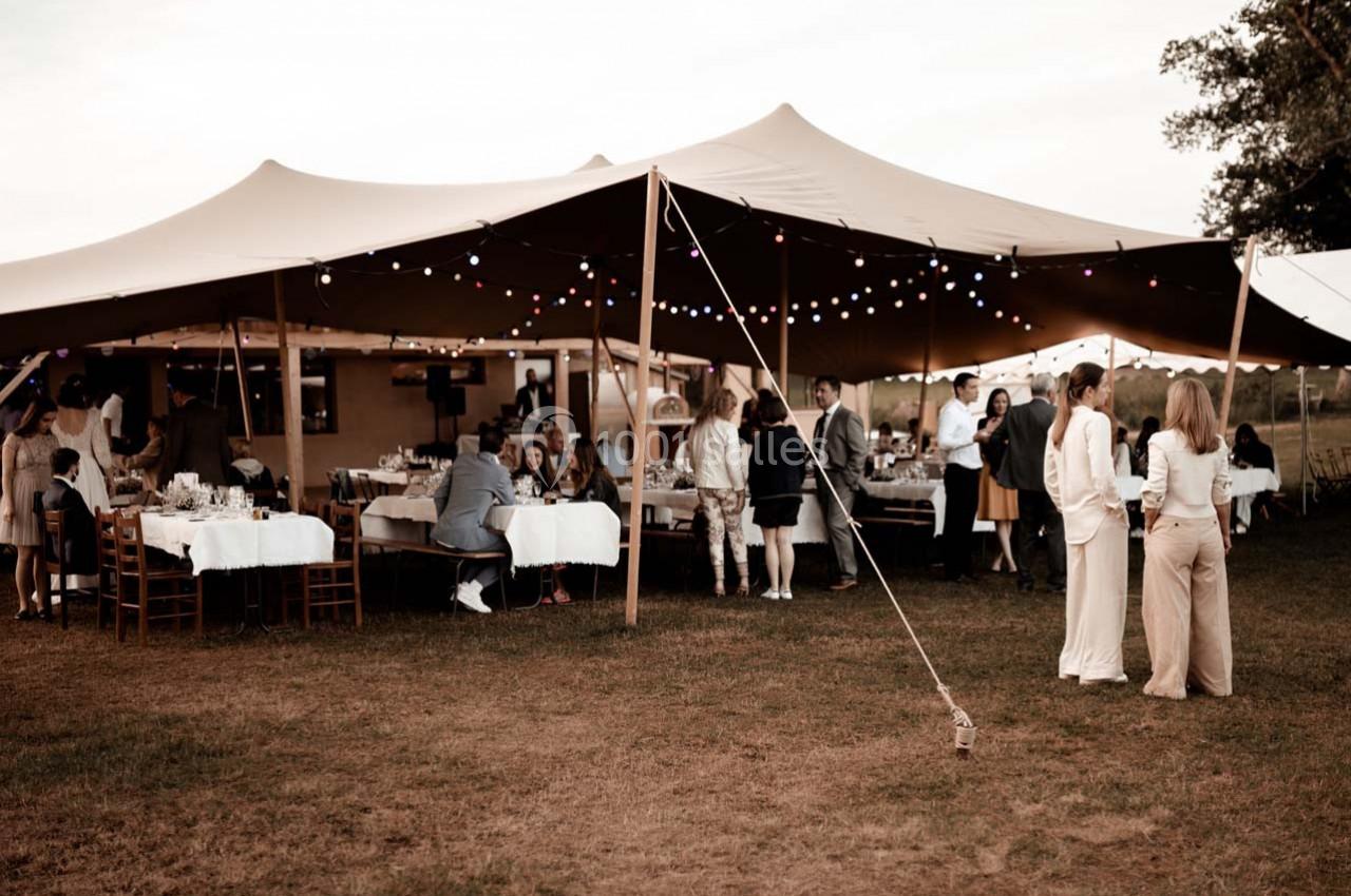 Des personnes rassemblées sous une grande tente éclairée, lors d'un événement en plein air sur une pelouse.