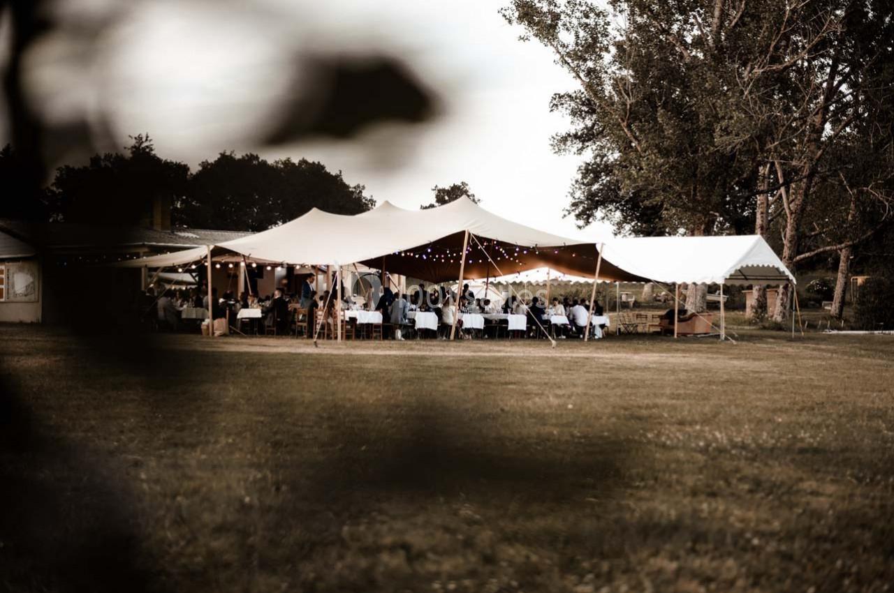 Tente blanche installée en extérieur avec des invités assis à des tables, entourée d'arbres et d'une pelouse.