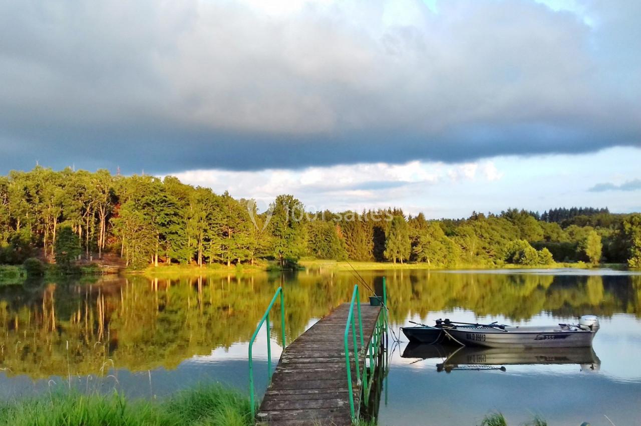 Ponton en bois menant à une barque amarrée sur un lac calme entouré de forêt sous un ciel partiellement nuageux.
