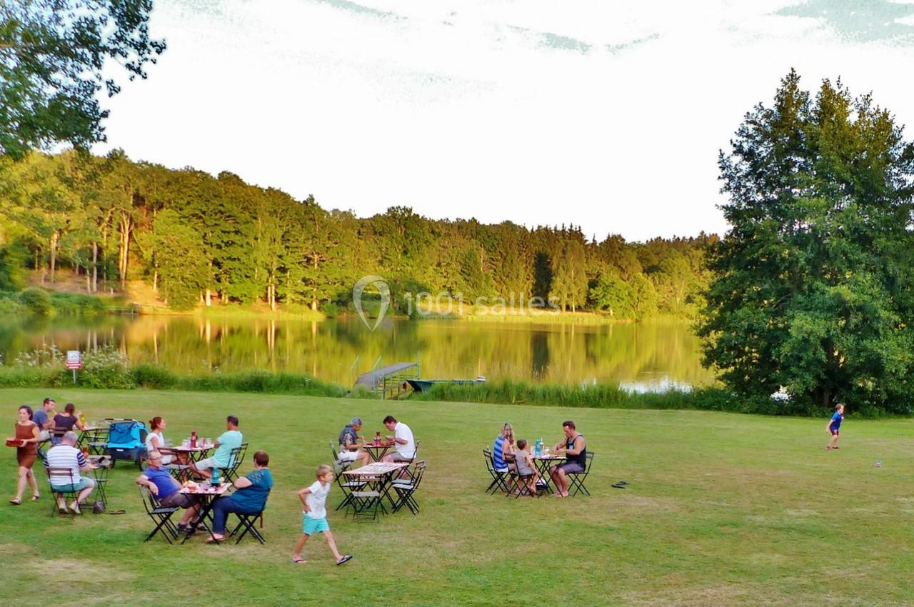 Des personnes dînent en plein air sur des tables disposées sur une pelouse près d'un lac entouré de forêt.