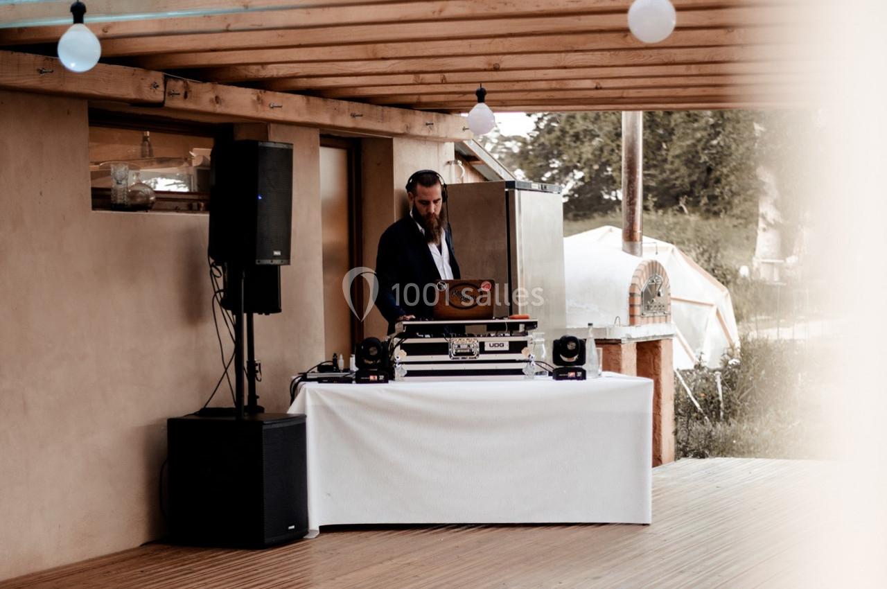 Un DJ mixant sur une table équipée de matériel audio sous une terrasse en bois, avec un extérieur verdoyant en arrière-plan.
