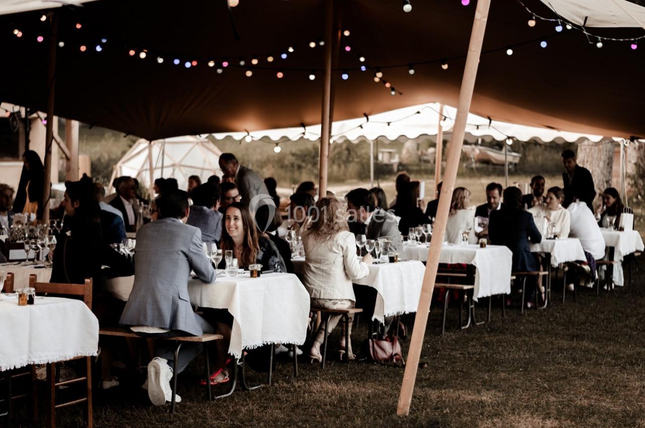 Des convives assis à des tables sous une tente éclairée par des guirlandes lumineuses, lors d'un événement en plein air.