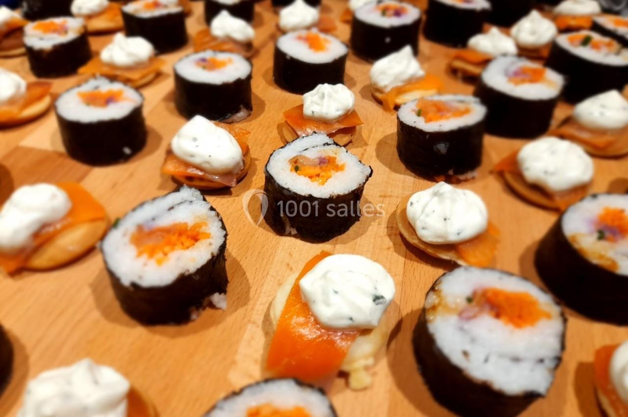 Assortiment de sushis et de bouchées au saumon garnies de crème, disposés sur une planche en bois.
