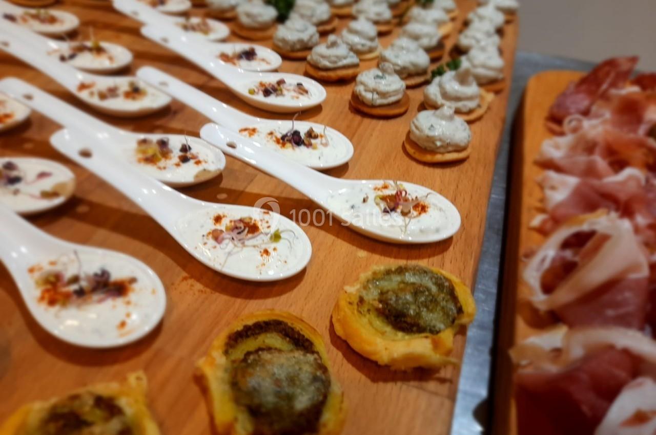 Assortiment de bouchées apéritives sur plateau en bois, incluant cuillères garnies, toasts et charcuterie.